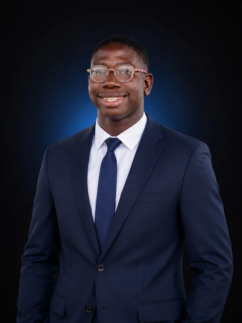 Portrait of Ebitimi Ebelike wearing a navy suit and glasses.